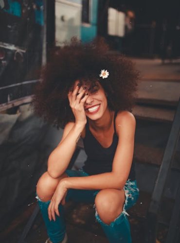 Cheerful woman wearing ripped jeans and curly hair with flower, enjoying a sunny day outdoors.